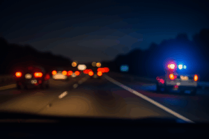 Night highway from driver’s view with blurred taillights and a police cruiser’s flashing lights.